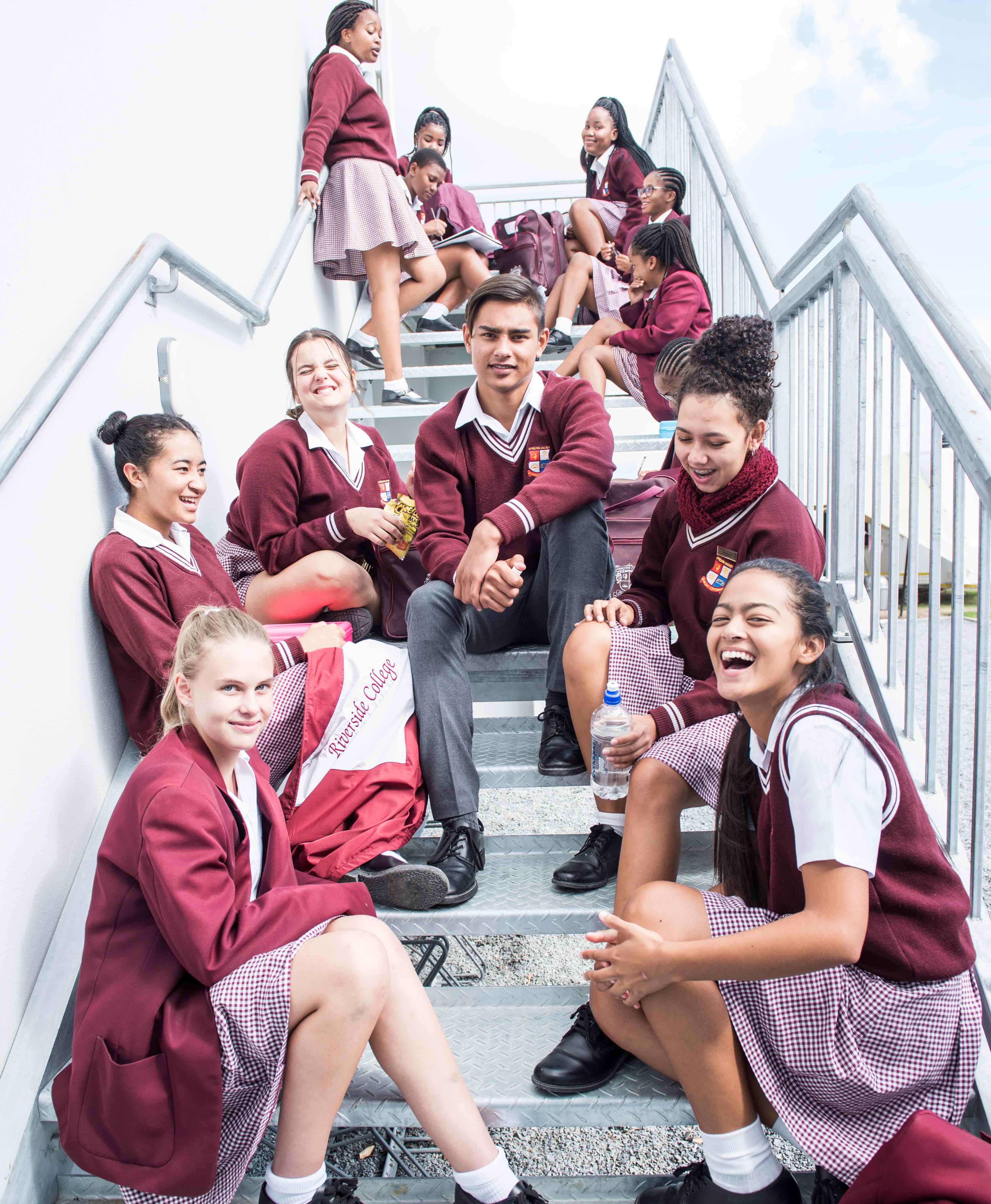 Riverside College High school learners sitting on a staircase, laughing and having fun during break time