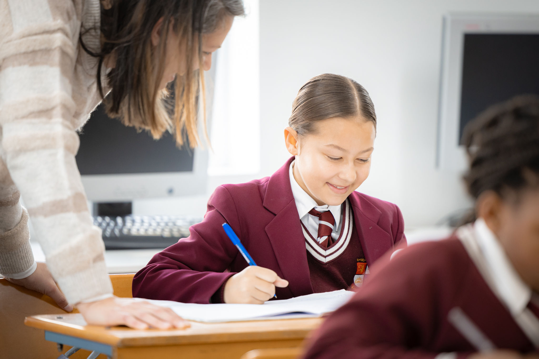 A Riverside College Primary school learner working in class while a teacher is assisting her